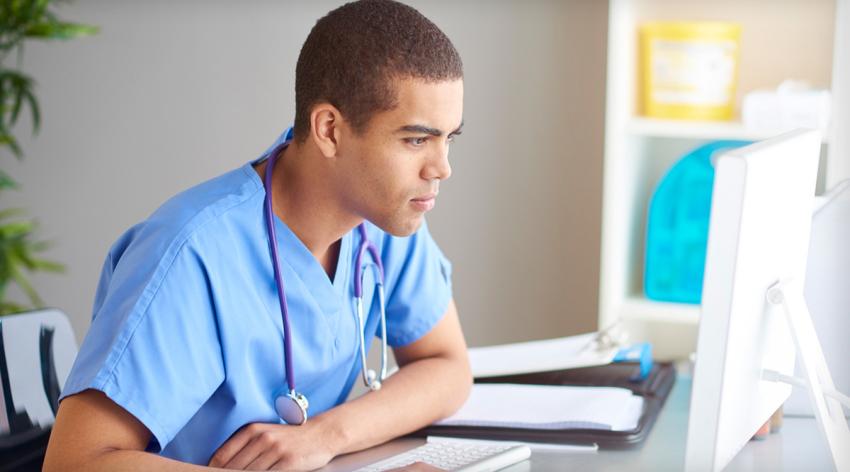 Nurse or doctor sitting at computer with stethoscope around neck