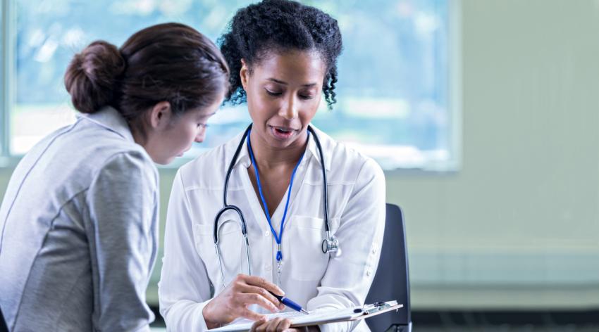 A female doctor talking to a colleague and pointing to something on a form attached to a clipboard