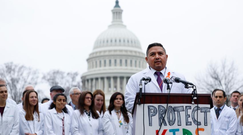 A physician speaks at a podium outside the Capitol building in Washington DC, surrounded by other doctors in white coats