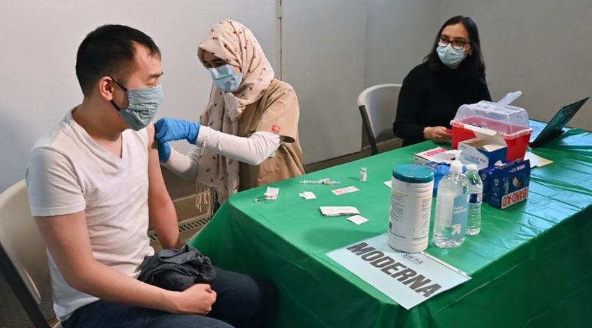 Justin Lau gets a bandage after his COVID-19 shot from UC Davis medical student Khadija Soufi at Shifa Community Clinic in Sacramento as undergraduate student Dana Hazem looks on.