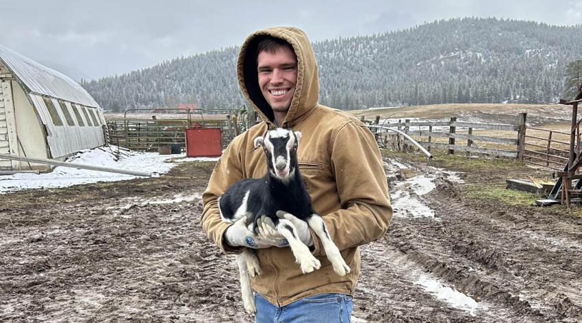 A student holds a goat on a farm