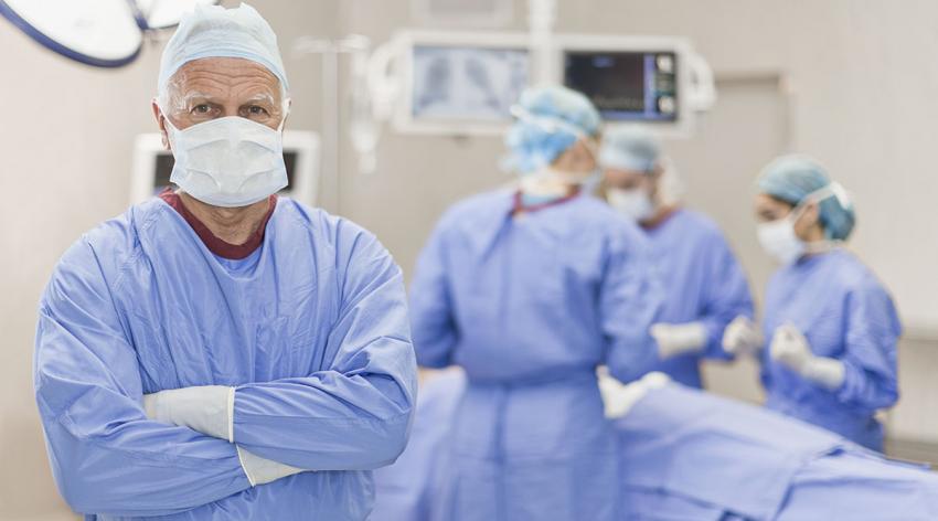 An older physician stands in an operating room wearing protective gear