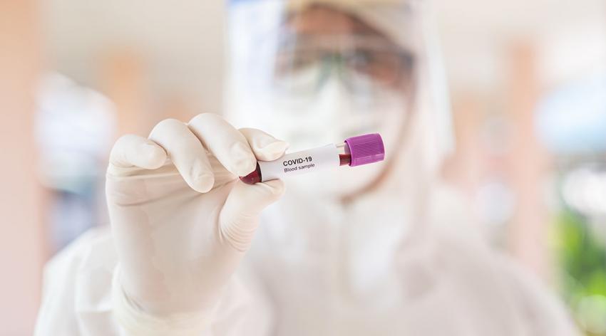 A researcher in protective gear holds a COVID-19 blood sample