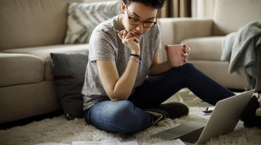 A woman sits on the floor and stares at her notes and laptop