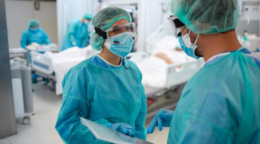 Two masked doctors in scrubs talk in a hospital room