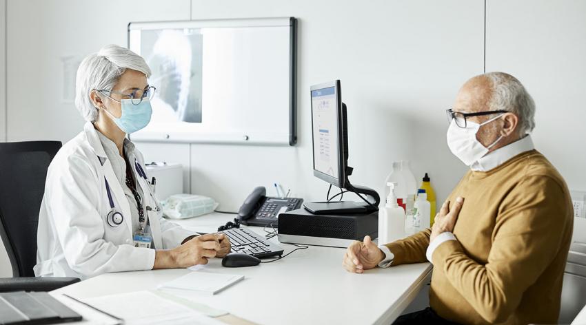 A masked doctor talks with a masked patient in her office