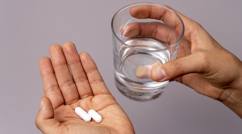 Elevated view of hand holding pills and a glass of water