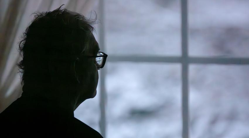 Lonely senior man looking out of window at winter 