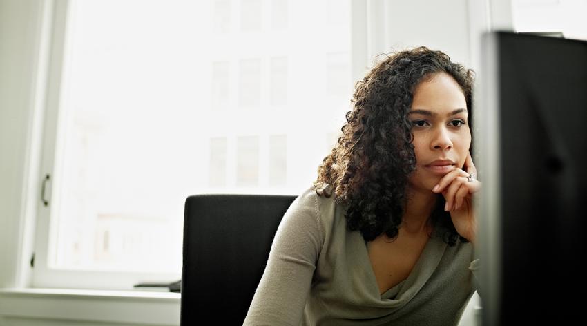 Businesswoman working on computer at workstation in office resting hand on chin