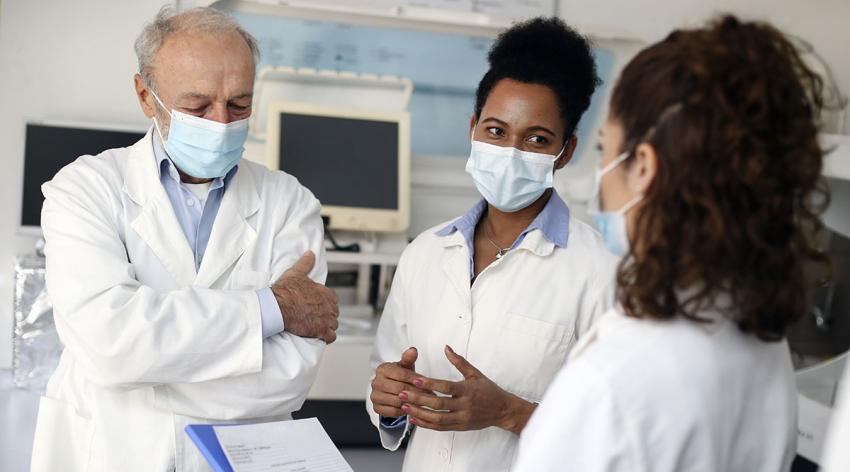 Team of scientists working in a lab during the pandemic - Caucasian senior male, Caucasian young woman and a Mixed race woman.