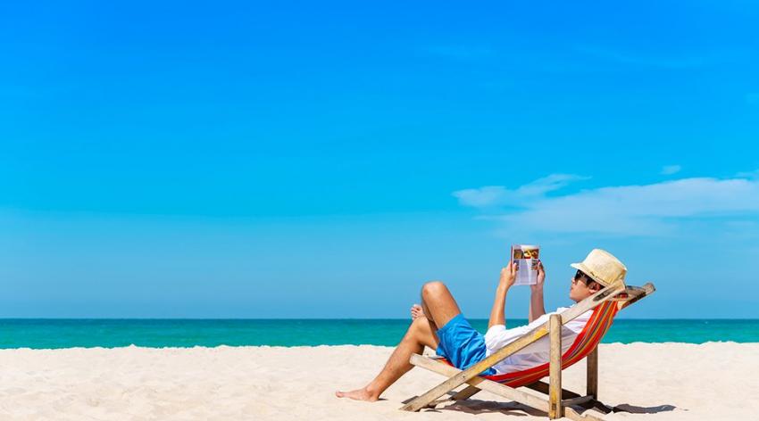 A man sitting on a beach chair near the water reading a book