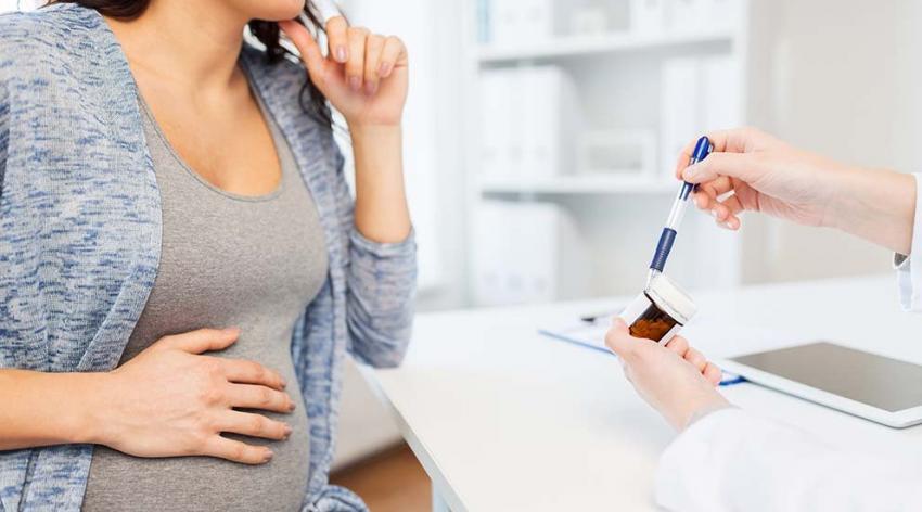 Pregnant woman being handed a prescription bottle by a medical worker who is not in the image