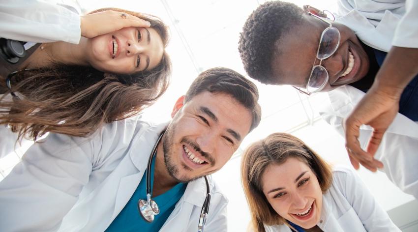 Group of people of 4 medical workers who are bending over looking down and laughing merrily