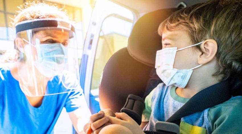 Female healthcare worker approaching a child boy in order to perform a Covid-19 test inside the car.