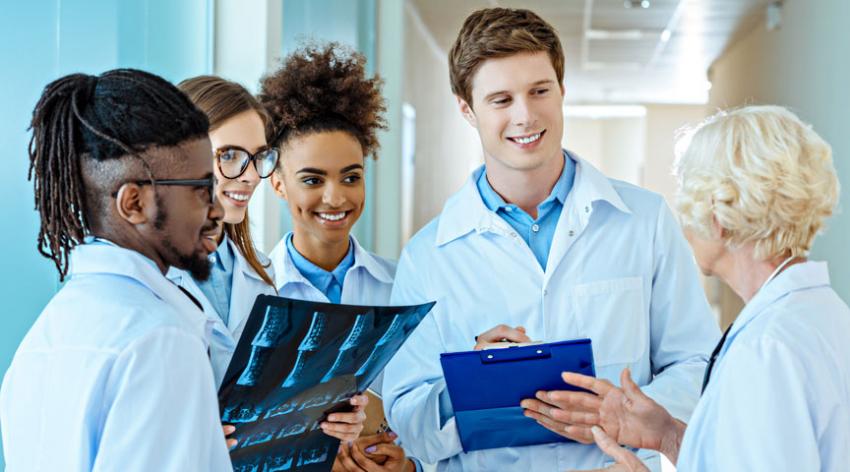 A diverse, young medical interns listening to a doctor in a hospital corridor.