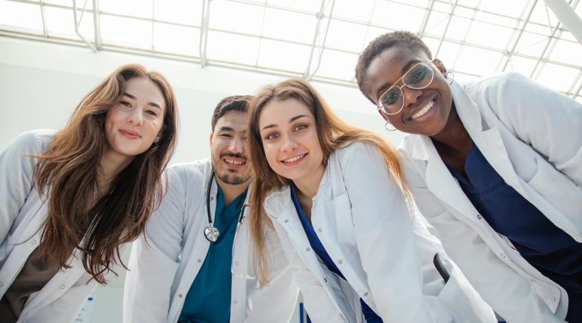 A group of four medical university students in white coats look down and smile