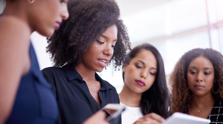 A group of women look together at a phone and a tablet.