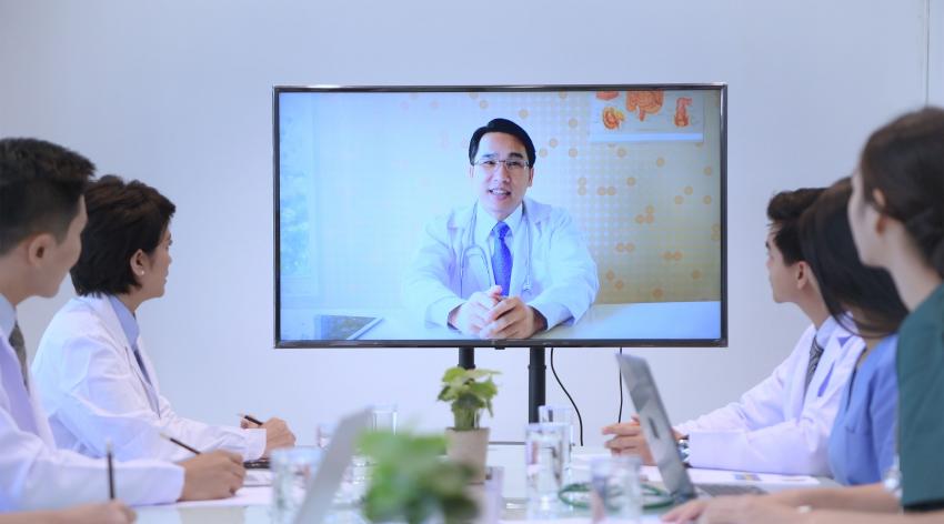 A male doctor teaches a group of fellow health professionals over the computer.