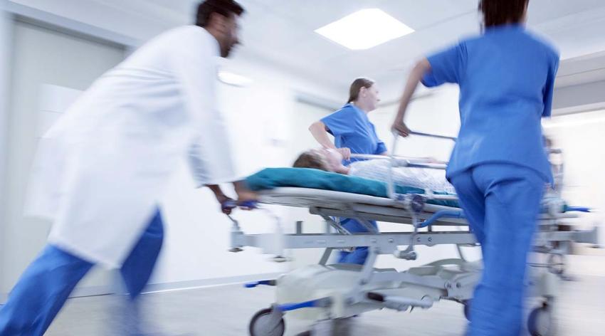 Doctors and medical workers quickly push a patient on a gurney through a hospital hallway. 