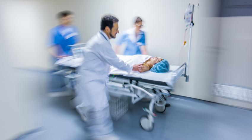 Medical staff wheeling a patient on stretcher in hospital's corridor.