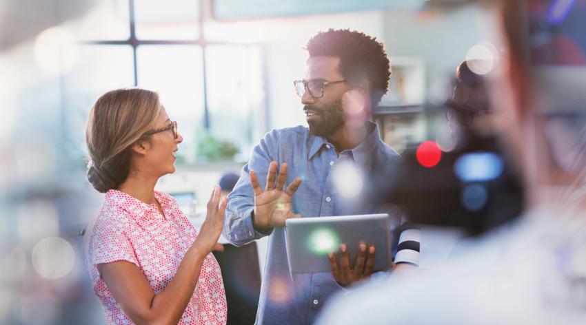 A female talking to a male colleague who is holding a laptop.