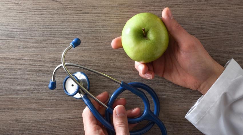 Nutritionist doctor with apple and stethoscope in hands on table
