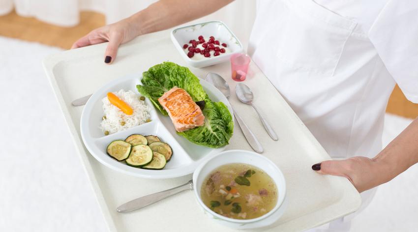 Young woman holding patient tray with main meal