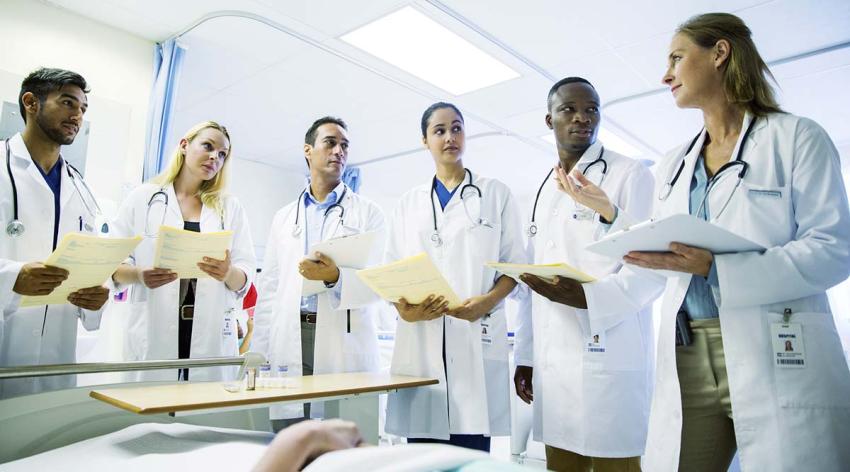 Five residents listen to a physician in a hospital room