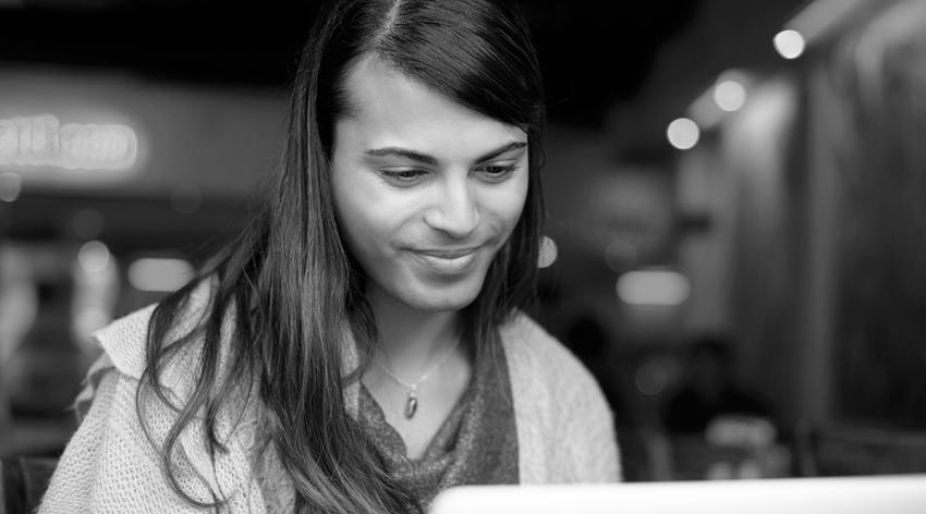 A young gender fluid person smiling while using a laptop in a cafe.