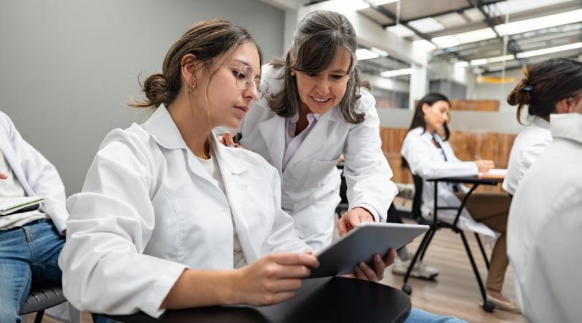 Latin American teacher helping a medical student in class and pointing at a digital tablet