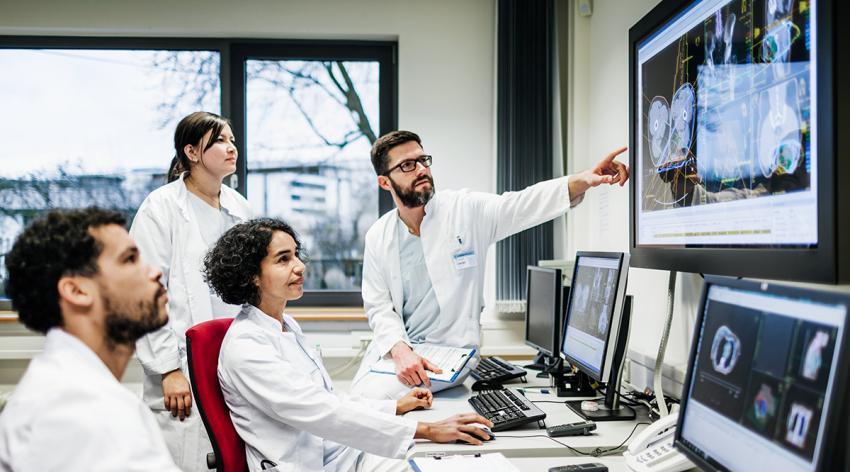 A team of doctors looking at some lab results together on monitors, in an office at the hospital.