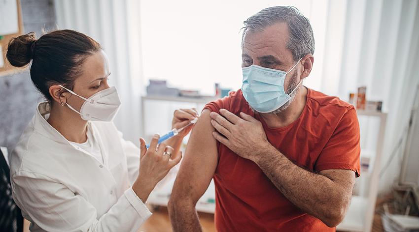 Young female doctor injecting COVID-19 vaccine in arm of senior man for coronavirus immunization.