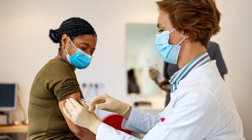 A masked patient receiving an injection from a masked medical professional