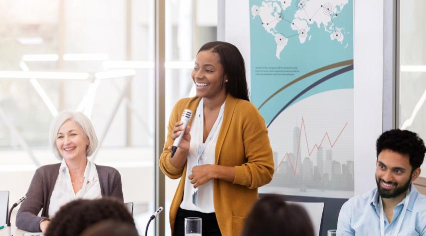 Woman holding microphone during a business meeting while coworkers sit at table