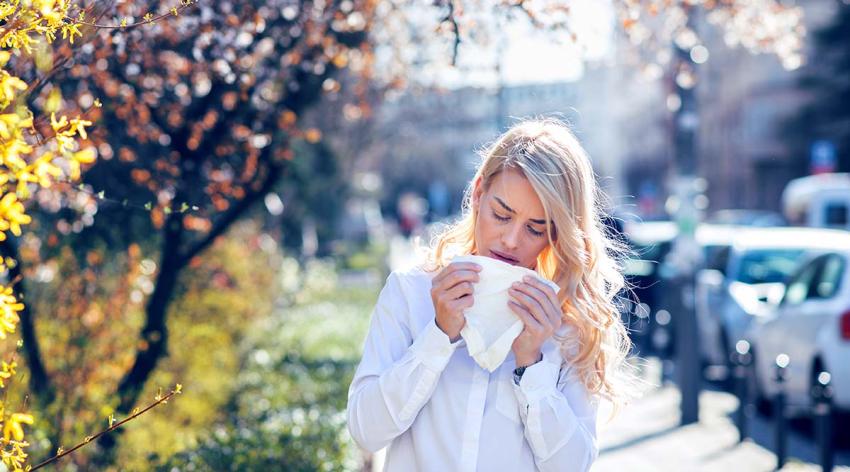 A woman holding a tissue near her face while standing outside near some trees