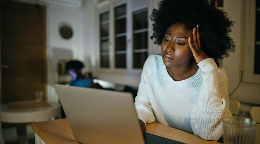 Tired, young woman sitting at the table and working from home late at night.