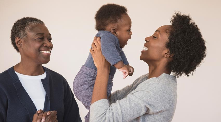 Young African woman holding baby boy with grandmother watching and smiling