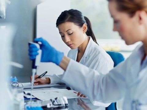 Two female doctors wearing white coats work side-by-side in a lab