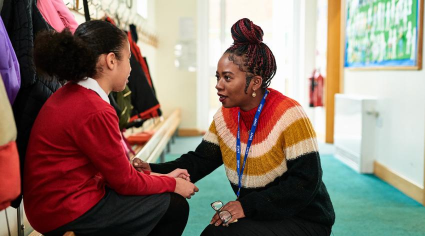 Primary school teacher supporting girl in coat room