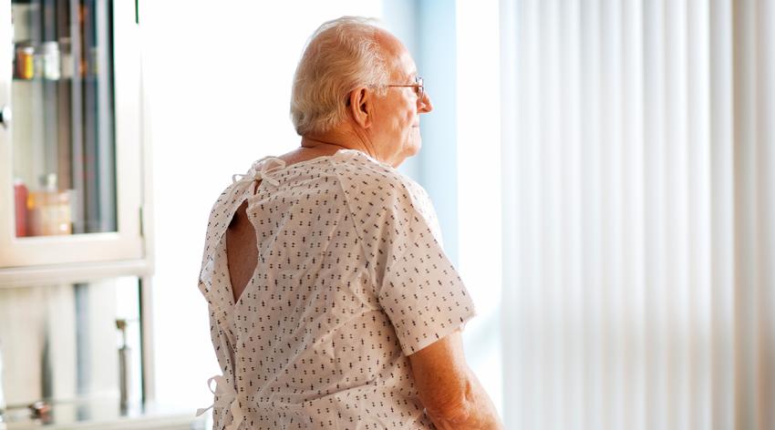 Senior man sitting in doctors office on examining table looking out window.